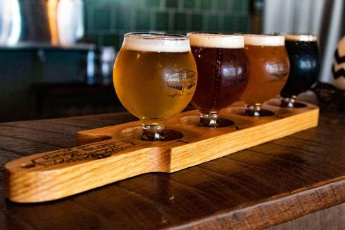A wooden flight paddle holds four different craft beer glasses, showcasing a variety of colors and styles.