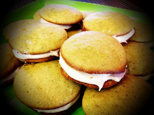 A close-up of greenish-yellow whoopie pies filled with white cream, arranged on a green plate.