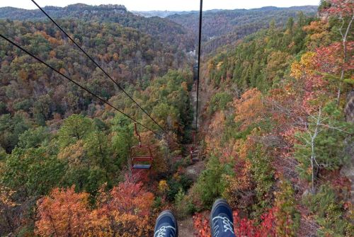 View from a chairlift overlooking a colorful autumn landscape with trees in shades of red, orange, and green.