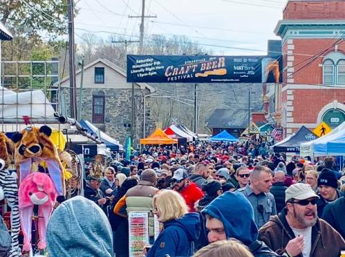 A bustling street festival with crowds, tents, and vendors, celebrating craft beer in a lively atmosphere.