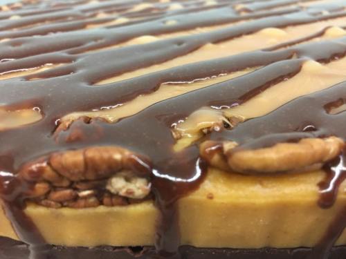 Close-up of a dessert with layers of caramel, chocolate drizzle, and pecans on top.