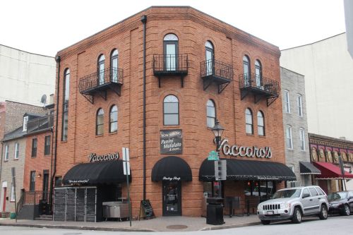 A brick building with arched windows and balconies, featuring a restaurant named "Vaccaro's" on the corner.