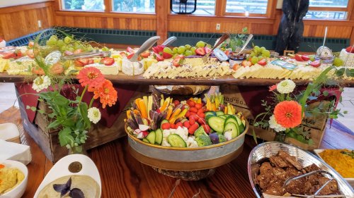 A beautifully arranged buffet featuring a variety of cheeses, fruits, vegetables, and dips, decorated with flowers.