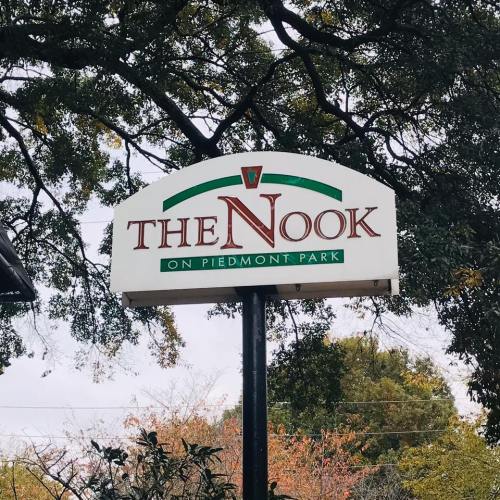 Sign for "The Nook on Piedmont Park" surrounded by trees, with a cloudy sky in the background.
