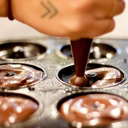A hand using a piping bag to fill a muffin tin with chocolate batter.
