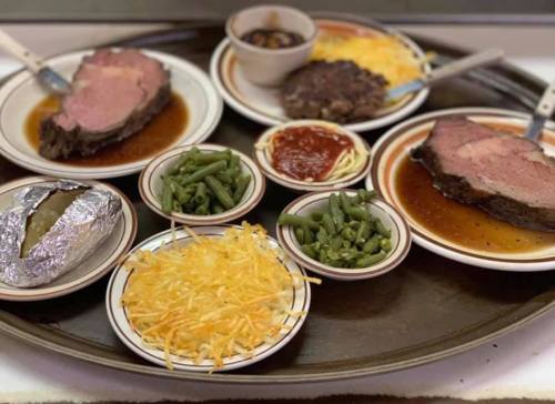A tray with two plates of sliced roast beef, sides of green beans, shredded cheese, baked potato, and spaghetti with sauce.
