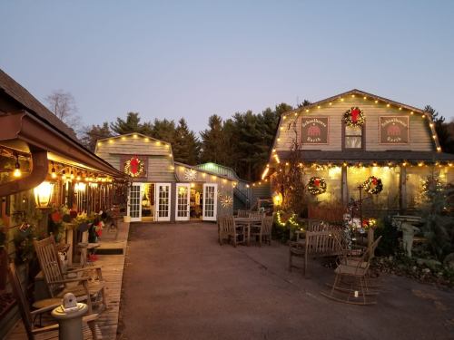 A cozy holiday scene featuring two decorated buildings with wreaths and string lights, surrounded by trees at dusk.