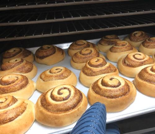 Freshly baked cinnamon rolls on a tray, with a hand reaching in from the side.