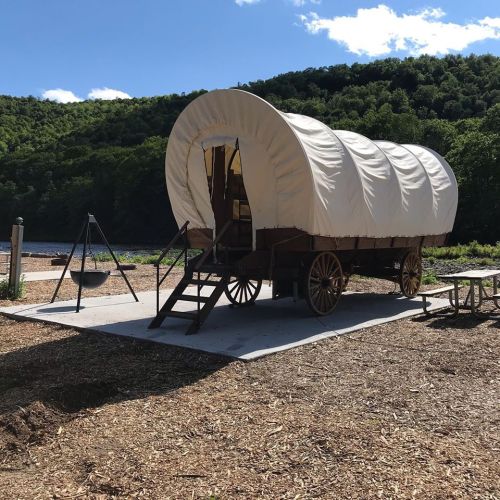 A covered wagon on a wooden platform, surrounded by trees and a clear blue sky.