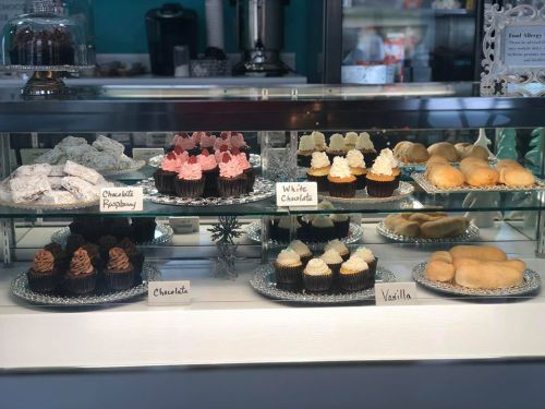 A display case filled with various cupcakes and pastries, labeled chocolate, white chocolate, raspberry, and vanilla.