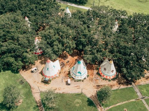 Aerial view of colorful teepees nestled among trees in a grassy area.