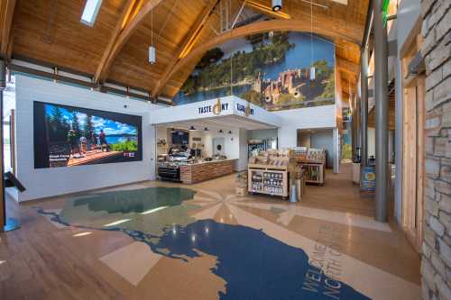 Interior of a visitor center featuring a large screen, a display counter, and a map on the floor. Bright, wooden architecture.