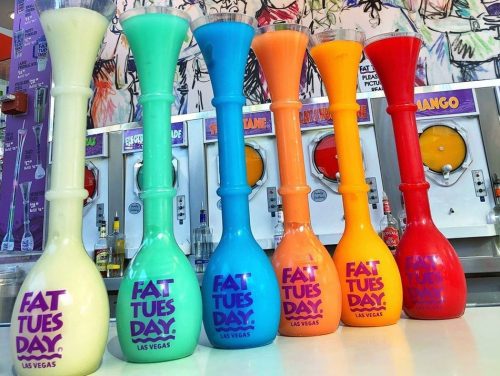 Colorful frozen drink towers in various shades, labeled "Fat Tuesday Las Vegas," lined up against a vibrant background.