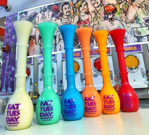 Colorful frozen drink towers in various shades, labeled "Fat Tuesday Las Vegas," lined up against a vibrant background.