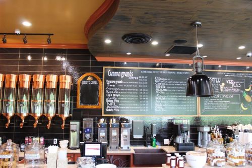 A cozy coffee shop interior featuring a menu board, coffee dispensers, and various brewing equipment.