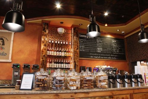 A cozy café counter with jars of baked goods, coffee machines, and a menu board in a warm, inviting atmosphere.