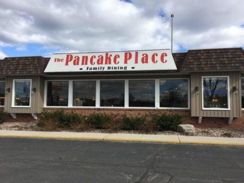 Exterior of The Pancake Place restaurant, featuring a large sign and windows, set against a cloudy sky.