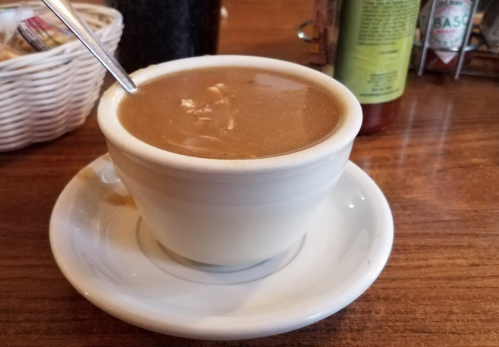 A white cup filled with brown soup or gravy, resting on a small white saucer on a wooden table.