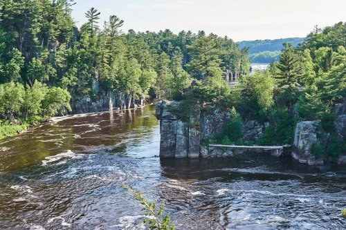 A scenic view of a river winding through lush green trees and rocky cliffs under a clear blue sky.