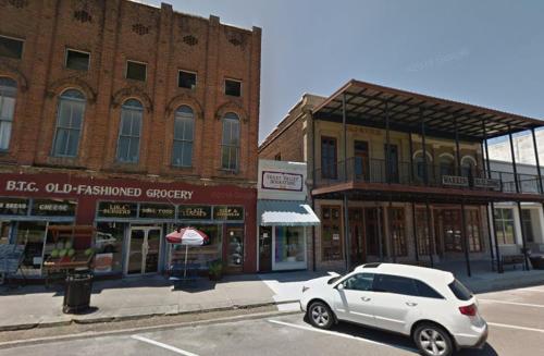 Historic buildings line a street, featuring a grocery store and a two-story structure with a balcony.