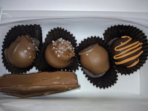A box of assorted chocolate truffles, including salted, drizzled, and plain varieties, in black paper liners.