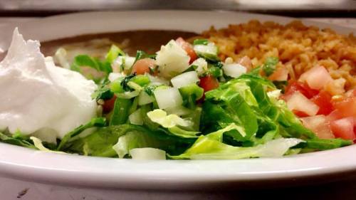A plate featuring rice, refried beans, and a fresh salad with lettuce, tomatoes, onions, and a dollop of sour cream.