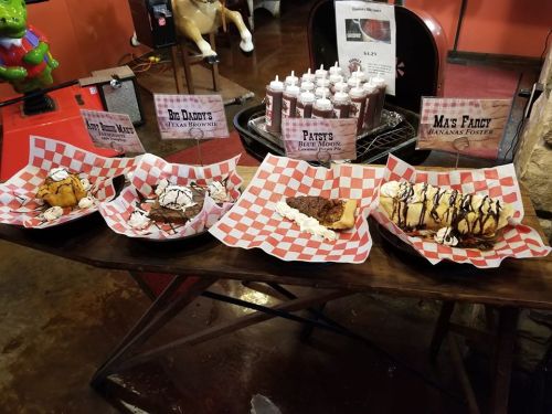 A display of four desserts on checkered plates: brownies, banana foster, and other sweet treats with toppings.