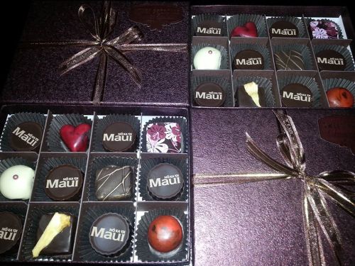 Two elegant chocolate boxes with assorted chocolates, including heart shapes and floral designs, tied with gold ribbons.