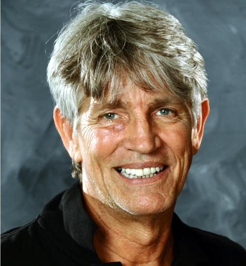 Smiling man with silver hair, wearing a black shirt, against a textured gray background.