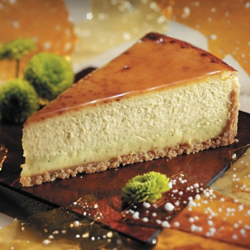A slice of creamy cheesecake with a glossy caramel topping, set on a decorative plate with a festive background.