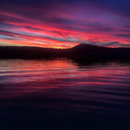A vibrant sunset with pink and purple hues reflecting on calm water, silhouetting a distant mountain.