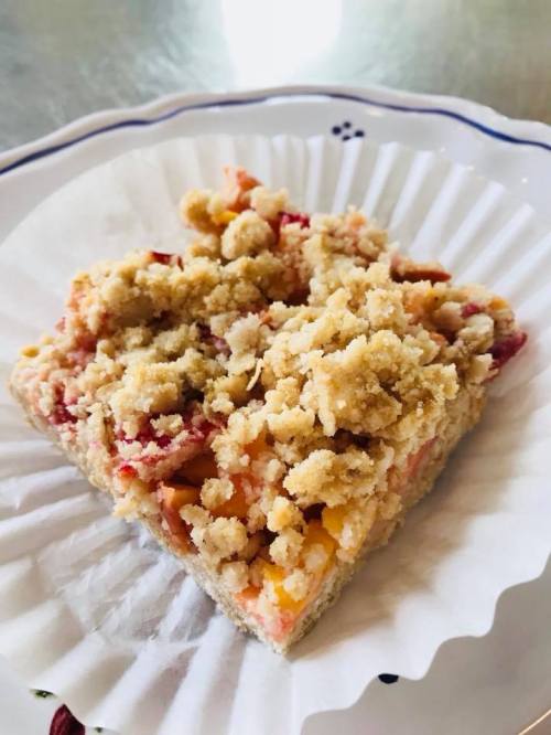 A slice of fruit crumble dessert on a paper liner, featuring a crumbly topping over a fruity filling.