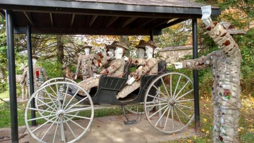 A whimsical sculpture of figures in a horse-drawn carriage, surrounded by artistic stone and glass decorations.