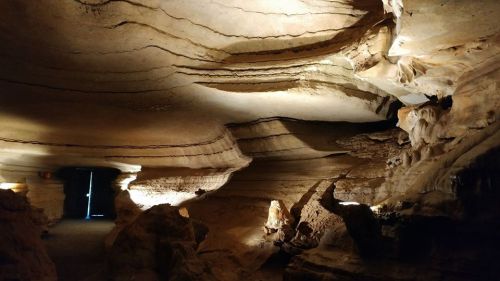 A dimly lit cave interior with textured rock formations and shadows, showcasing natural layers and contours.