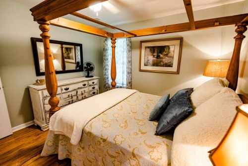 Cozy bedroom featuring a four-poster bed, decorative quilt, wooden furniture, and soft lighting.