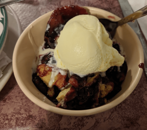 A bowl of dessert featuring warm berry cobbler topped with a scoop of vanilla ice cream.