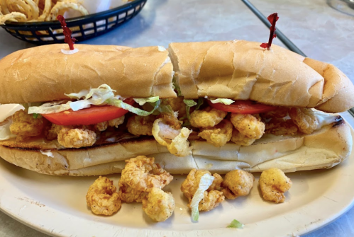 A sandwich filled with shrimp, lettuce, and tomato, served on a toasted hoagie roll, with some shrimp scattered on the plate.