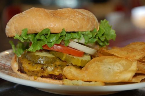 A juicy hamburger with lettuce, tomato, pickles, and cheese, served with a side of crispy potato chips.