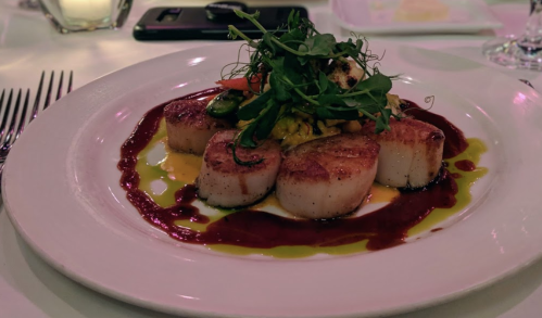 A plate of seared scallops garnished with microgreens, served with colorful sauces and a vegetable medley.