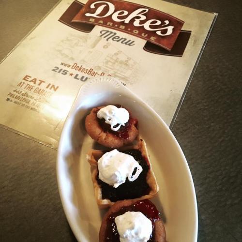 A dish of three mini desserts topped with whipped cream, served on a white plate next to a menu for Deke's Barbecue.