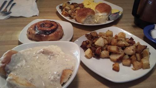 A hearty breakfast spread featuring biscuits, gravy, cinnamon roll, scrambled eggs, and seasoned potatoes.