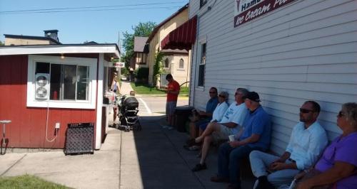A group of people sitting outside an ice cream shop, with a small service window and a stroller nearby.
