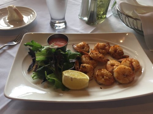 A plate of grilled shrimp with a side salad, lemon wedge, and dipping sauce, served on a white tablecloth.