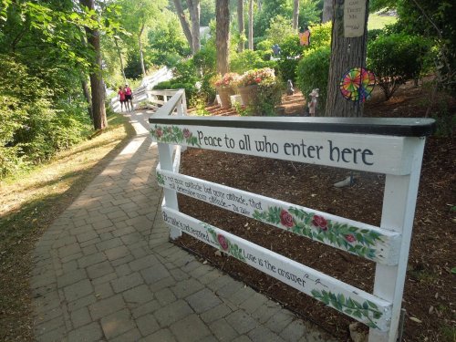 A pathway with a white fence adorned with flowers, welcoming visitors with a message of peace and love.