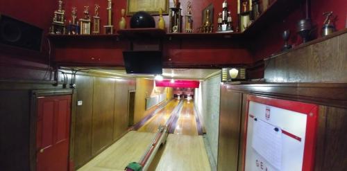 A view of a bowling alley with wooden lanes, trophies on the wall, and a monitor above the lanes.