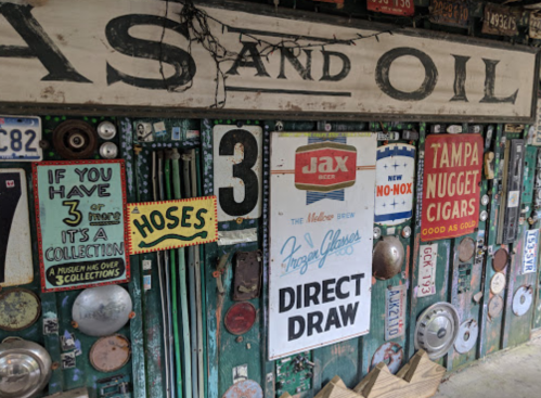 A colorful display of vintage signs, license plates, and memorabilia on a wooden wall, featuring various advertisements.