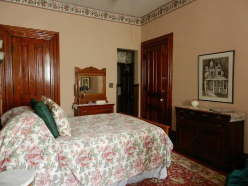 Cozy bedroom with floral bedding, wooden furniture, and vintage decor, featuring a mirror and a door leading outside.