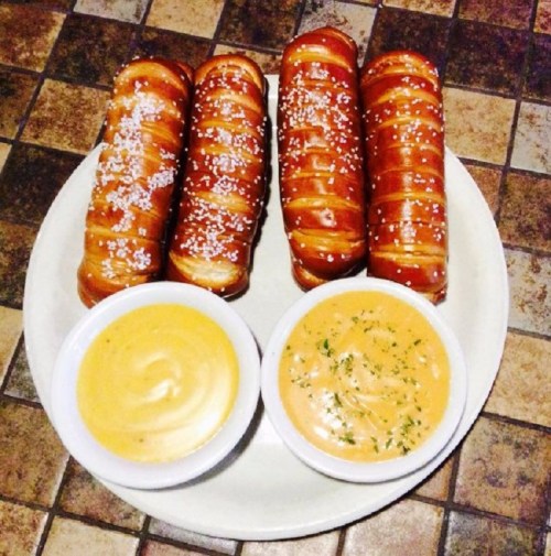 A plate with four twisted pretzels and two bowls of creamy dipping sauces.