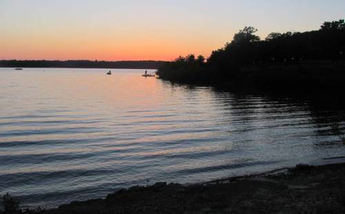A serene lake at sunset, with gentle waves and silhouettes of trees along the shore.