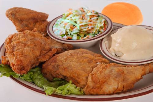A plate of fried chicken with coleslaw, mashed potatoes, and a roll, served on a bed of lettuce.